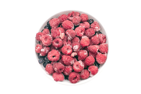 Frozen delicious raspberries lie in the middle on a light isolated background, close-up top view.