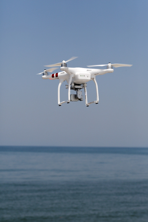 KAGAWA, JAPAN-MAY 20, 2016: White remote controlled Drone Dji Phantom 3 equipped with high resolution video camera hovering in air with beach and blue skyのeditorial素材