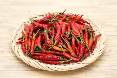 Dried red chili pepper plants in bamboo basket on wooden tableの写真素材