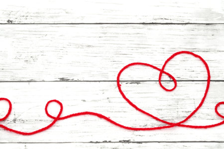Red woolen thread in the shape of heart on white wooden tableããの写真素材