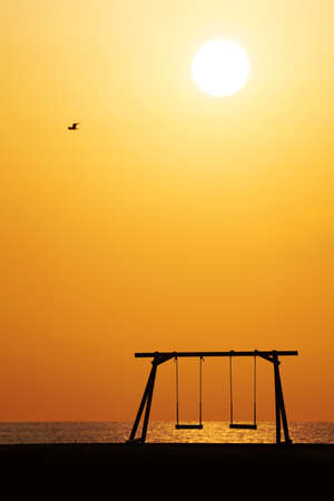 Silhouette of wooden swing with beautiful sunset on the hill near the seaの写真素材