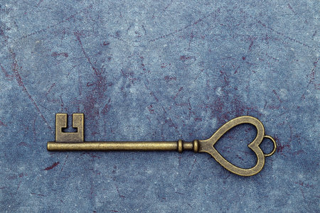 golden heart shaped vintage key on a grungy blue leather backgroundの写真素材