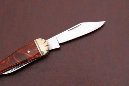 Close up photo of small folding knife on red leather backgroundãの写真素材