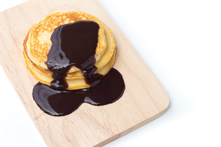 Pancakes with chocolate syrup on a wood plate and isolated on white backgroundの写真素材