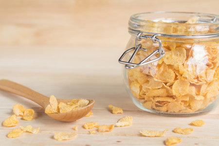 cereal cornflakes in the glass jar and spilling out to the wood table