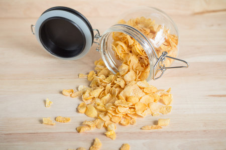 cereal cornflakes spilling out from the glass jar to wood surface