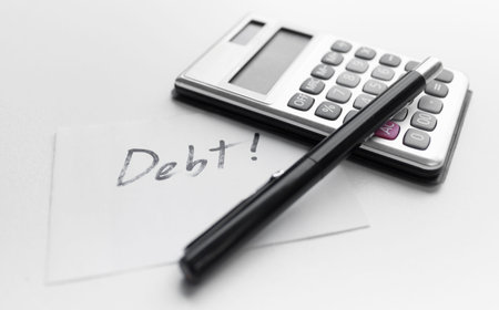Calculator with a pen and paper note with word debt isolated on white background