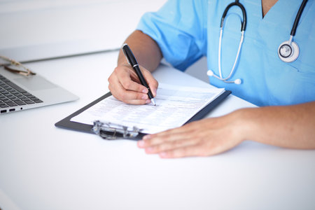 Portrait of unknown male surgeon doctor holding his stethoscope and filling up medical prescriptionの写真素材