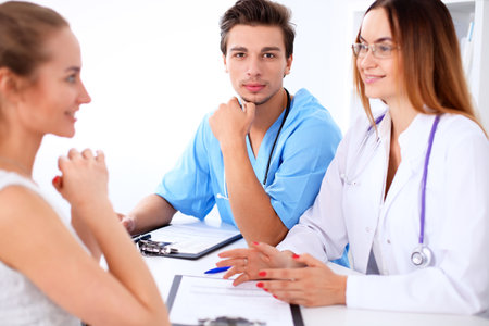 Attractive male doctor surgeon near female doctor and patient discussing, sitting at the deskの写真素材