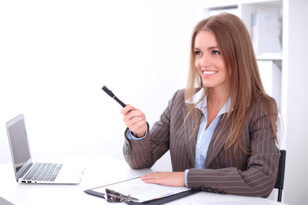 young business woman pointing into copy space by pen sitting at the desk on office backgroundの写真素材