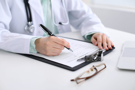 Close-up of a female doctor filling out application form , sitting at the table in the hospital.