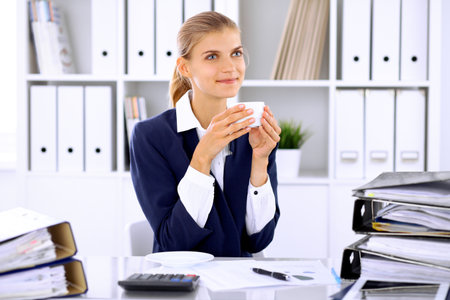 Happy business woman or female accountant having some minutes for coffee and pleasure at working placeの写真素材