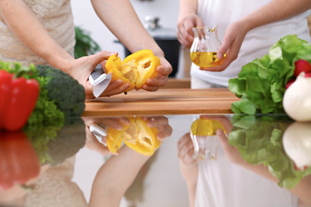 Closeup of two women are cooking in a kitchen. Friends having fun while preparing fresh saladの写真素材