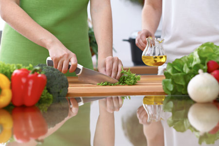 Closeup of two women are cooking in a kitchen. Friends having fun while preparing fresh saladの写真素材