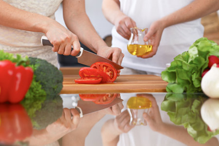 Closeup of two women are cooking in a kitchen. Friends having fun while preparing fresh saladの写真素材