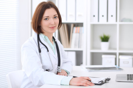 Young brunette female doctor sitting at the table and working at hospital office.の写真素材
