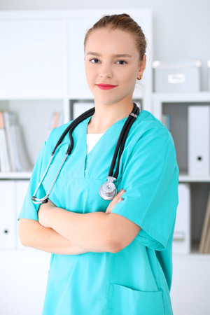 Female surgeon doctor is standing with arms crossed and smiling at hospital.  Physician ready to examine patientの写真素材