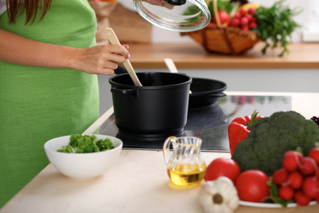 Young woman is cooking by the stove in the kitchen, close up.の写真素材