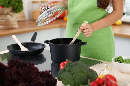 Young woman is cooking by the stove in the kitchen, close up.の写真素材