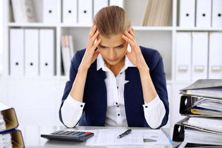 Tired business woman or female accountant with bills and paper folders in officeの写真素材