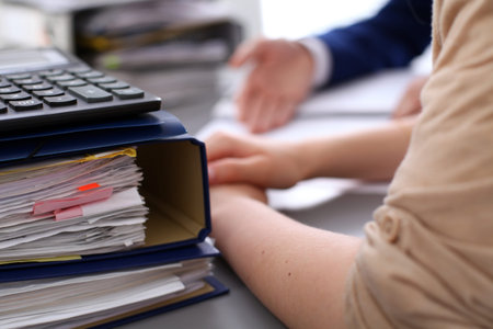 Binders with papers are waiting to be processed with businessman and secretary back in blur....