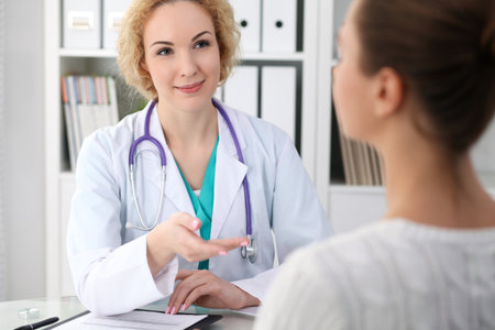 Happy blonde female doctor and patient discussing medical examination results. Medicine, healthcare and help conceptの写真素材