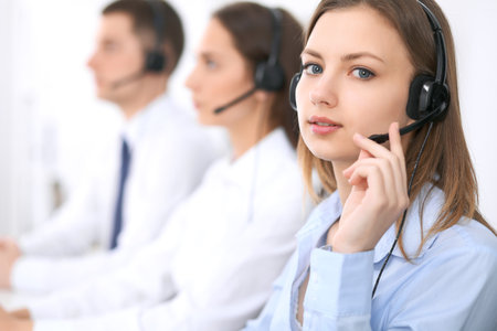 Call center operators. Focus at young beautiful business woman in headsetの写真素材
