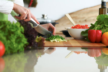 Closeup of human hands cooking vegetables salad in kitchen on the glass table with reflection. Healthy meal and vegetarian conceptの写真素材