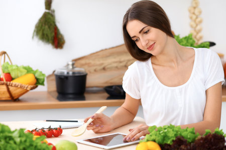 Beautiful Hispanic woman is making online shopping by tablet computer and credit card or searching internet for a new recipe. What to cook for a dinner.の写真素材