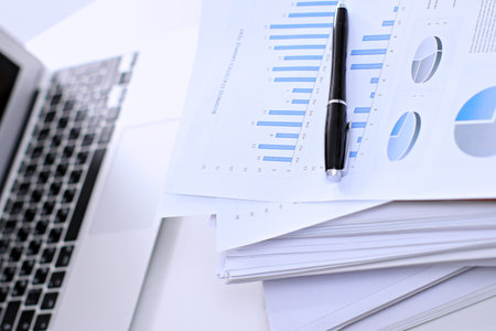 Office workplace with a laptop and financial documents on the light reflecting tableの写真素材