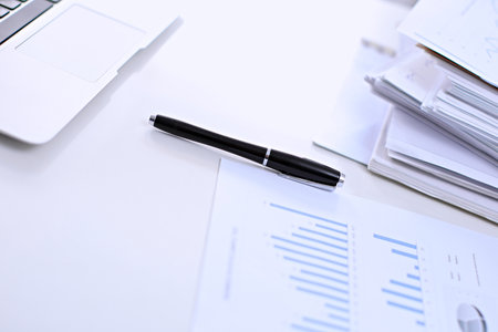 Office workplace with a laptop and financial documents on the light reflecting tableの写真素材