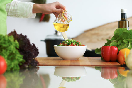 Closeup of human hands cooking vegetables salad in kitchen on the glass  table with reflectionの写真素材