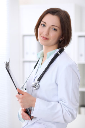 Young brunette female doctor standing with arms crossed and smiling at hospitalの写真素材