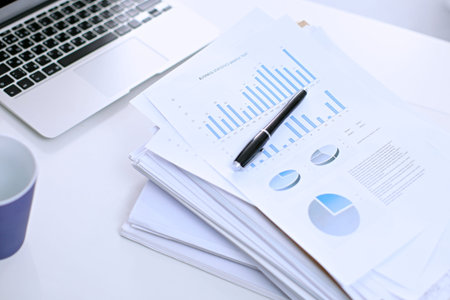 Office workplace with a laptop and financial documents on the light reflecting tableの写真素材