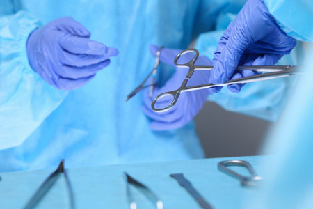 Close-up of of surgeons hands at work in operating theater toned in blue. Medical team performing...
