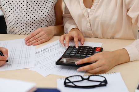 Two female accountants counting on calculator income for tax form completion hands closeup. Internal...