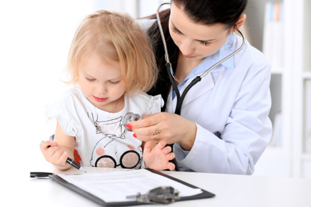 Pediatrician is taking care of baby in hospital. Little girl is being examine by doctor with stethoscope. Health care, insurance and help concept.の写真素材