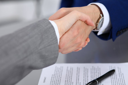 Businessman and business woman shaking hands to each other above signed contractの写真素材