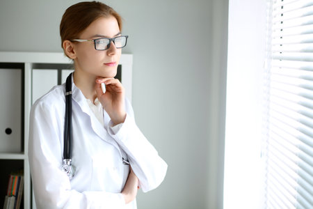Young brunette female doctor standing with arms crossed and smiling at hospital.  Physician ready to examine patientの写真素材