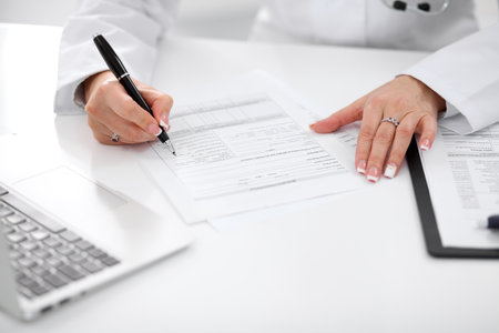 Close-up of a female doctor filling out application form , sitting at the table in the hospital.の写真素材