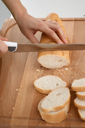 Close up of womans hands cooking in the kitchen. Housewife slicing white bread.の写真素材