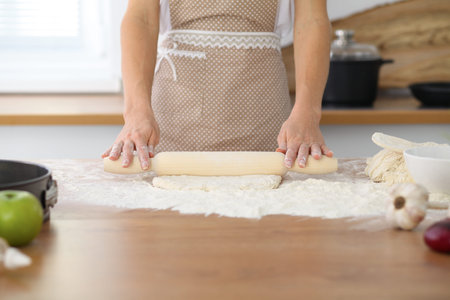 Female hands making dough for pizza or bread while using rolling pin. Baking concept.