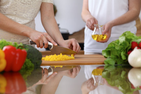 Closeup of human hands cooking in kitchen. Mother and daughter or two female cutting bell pepper for fresh salad. Healthy meal, vegetarian food and lifestyle conceptsの写真素材