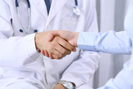 Male doctor and woman patient shaking hands. Partnership in medicine, trust and medical ethics conceptの写真素材
