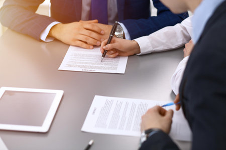 Group of business people and lawyer discussing contract papers sitting at the table, closeup. Businessman is signing document after agreement doneの写真素材
