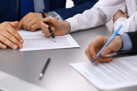 Group of business people and lawyer discussing contract papers sitting at the table, closeup. Businessman is signing document after agreement doneの写真素材