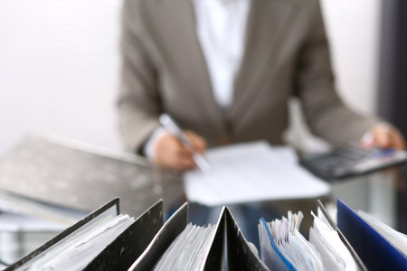 Binders with papers are waiting to be processed with businesswoman or secretary back in blurの写真素材