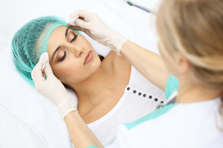 Professional beautician and young woman in beauty salon. Makeup artist touch  customer skin with cotton pads, closeup. Cosmetology , facial, beauty and spaの写真素材