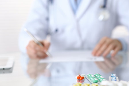 Medicine pills closeup with doctor writing prescription form back in blur.  Healthcare, insurance and excellent service in medicine conceptの写真素材