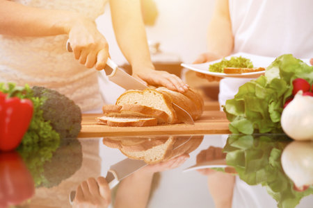 Closeup of human hands cooking in kitchen. Mother and daughter or two female friends cutting bread. Healthy meal, vegetarian food and lifestyle conceptの写真素材